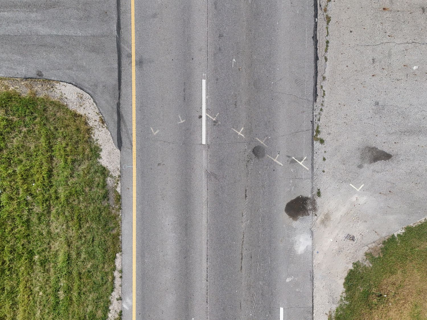 Top-down view of a roadway with paint markings and dark fluid stains at a vehicle's point of rest