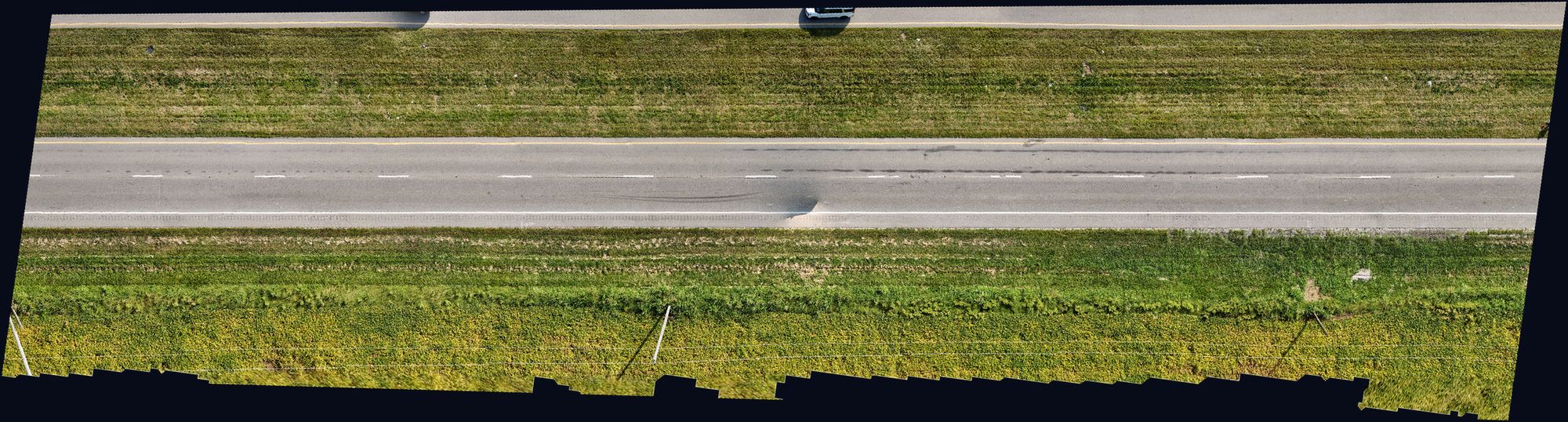 Top-down orthomosaic of a two-lane highway segment with visible tire marks across the travel lanes